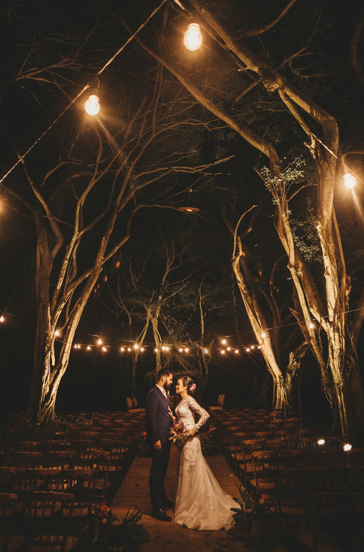 Couple under trees strung with warm lights at night